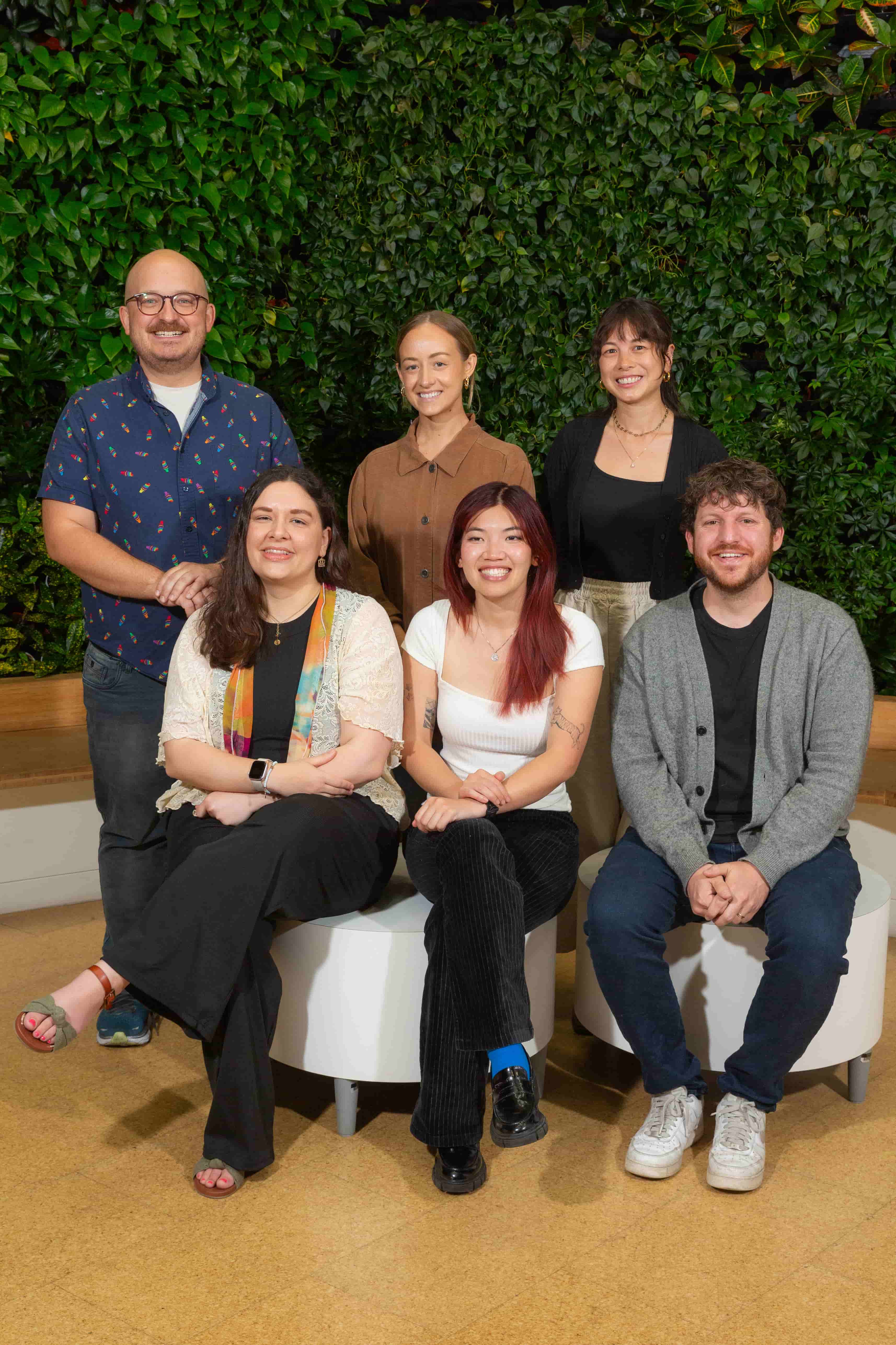 Five members of the Compiler Customer Success team pose smiling in front of a wall of greenery.